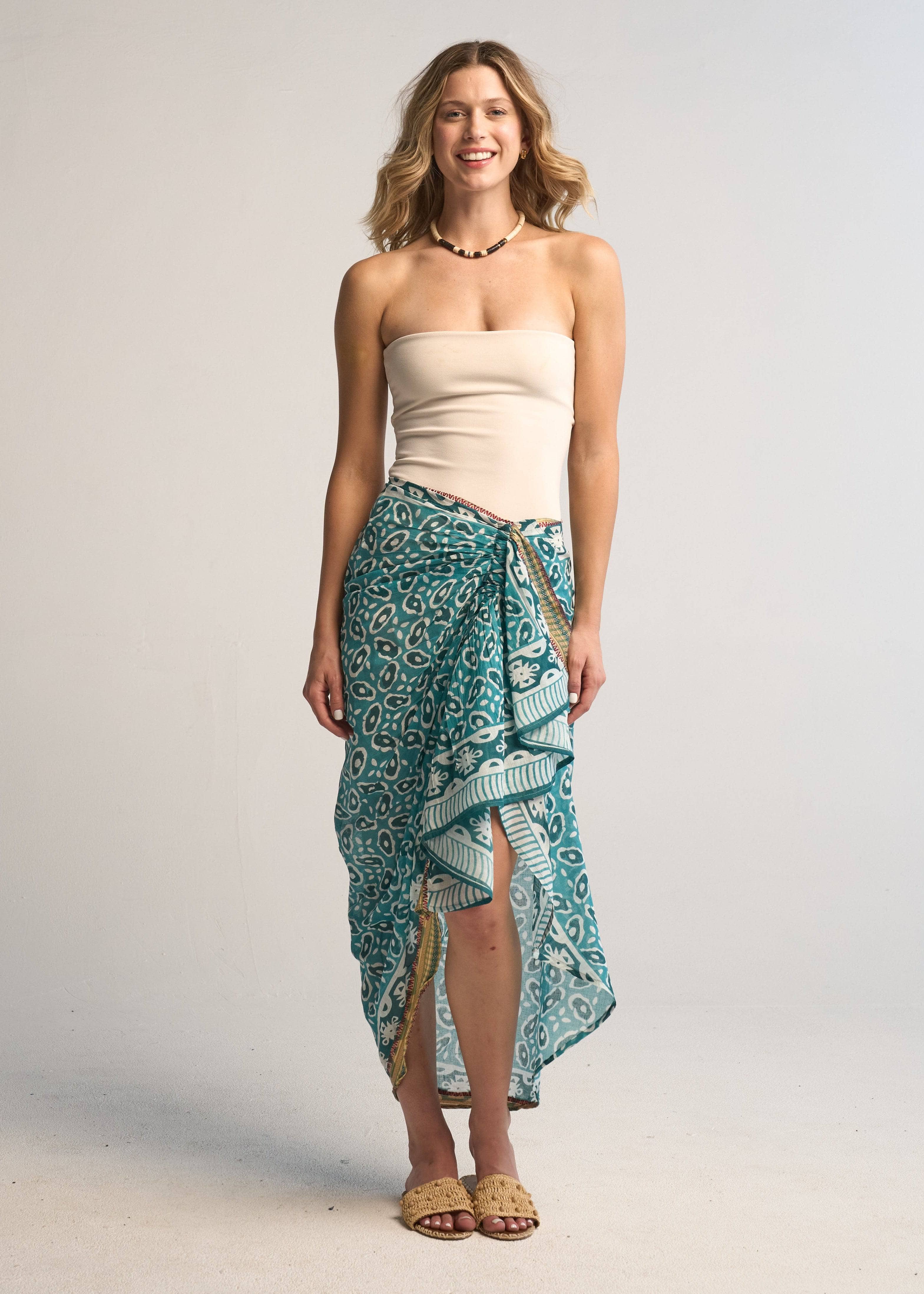 Woman wearing a strapless top and teal patterned sarong on a plain background